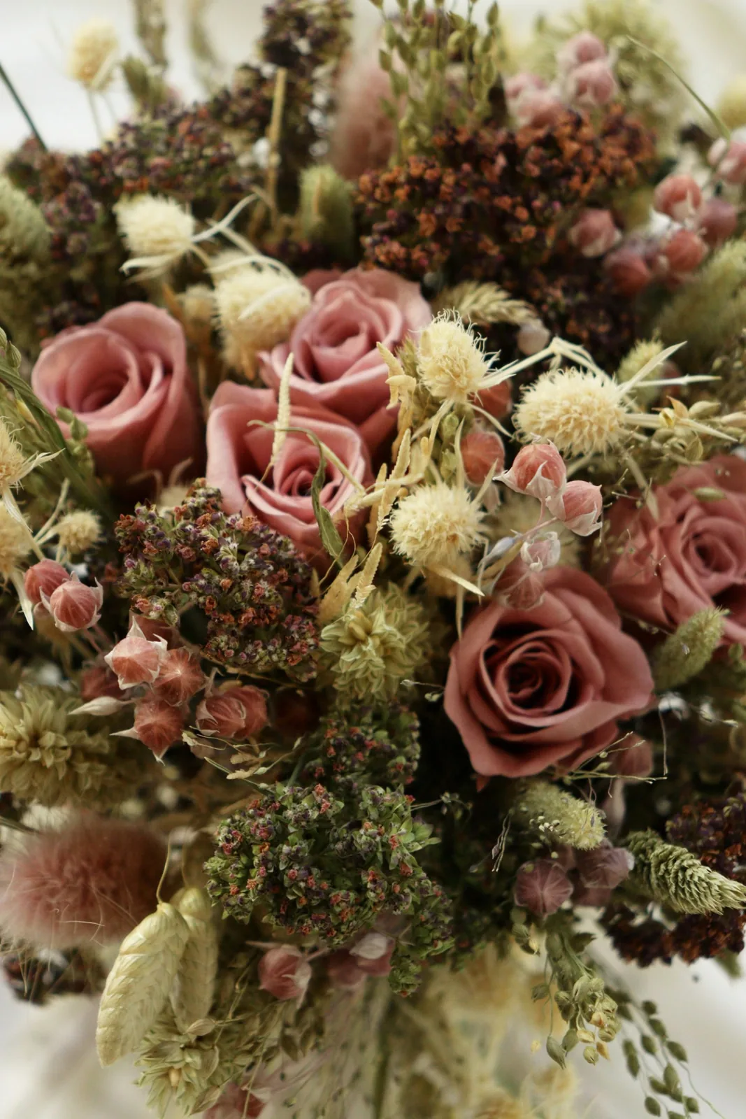 Primo piano di rose stabilizzate rosa antico con piccoli fiori essiccati e foglie verdi